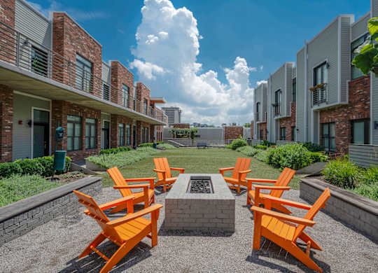 A row of orange chairs are arranged in a circle around a fire pit.
