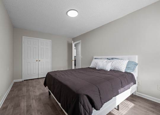 A bedroom with a bed, pillows, and a wooden floor.