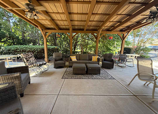 A covered patio with a couch, chairs, and a fan.