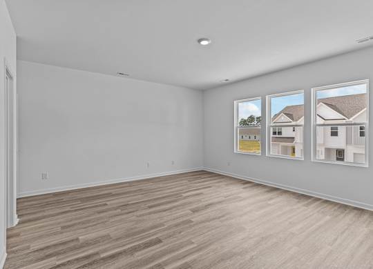 A large empty room with wood flooring and three windows.