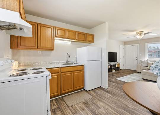 A kitchen with a white stove top oven and a white refrigerator with wooden cabinets.