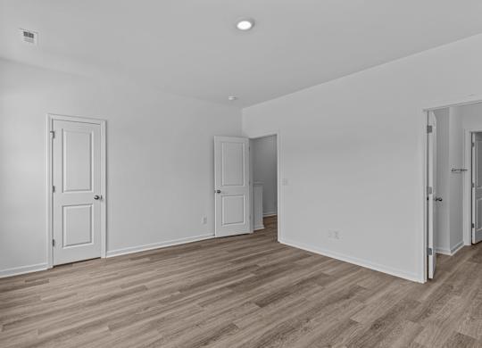 A room with white walls and wooden flooring with four doors.