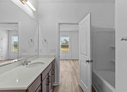 A white bathroom with a sink, mirror, and a door leading to another room.