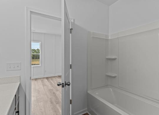 A white bathroom with a tub and a doorway leading to another room.