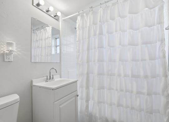 A white bathroom with a white sink and a white shower curtain.