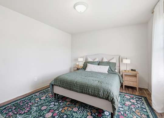 A bedroom with a bed, nightstand, and floral rug.