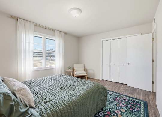 A bedroom with a bed, chair, and a window.