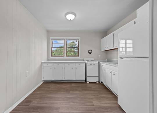 A white kitchen with wood flooring and white cabinets.