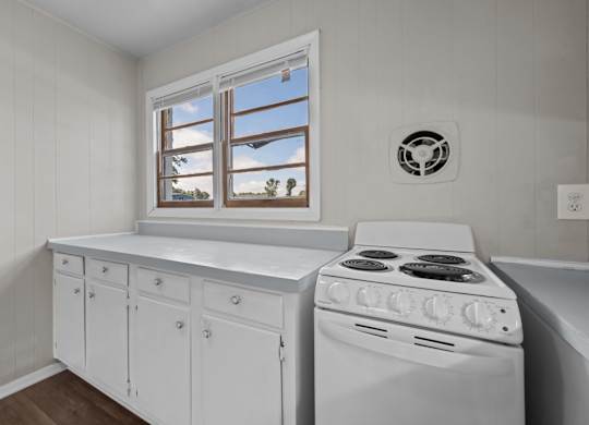 A white kitchen with a stove and a window.
