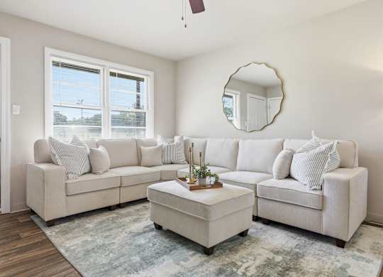 A living room with a white couch and a round mirror on the wall.
