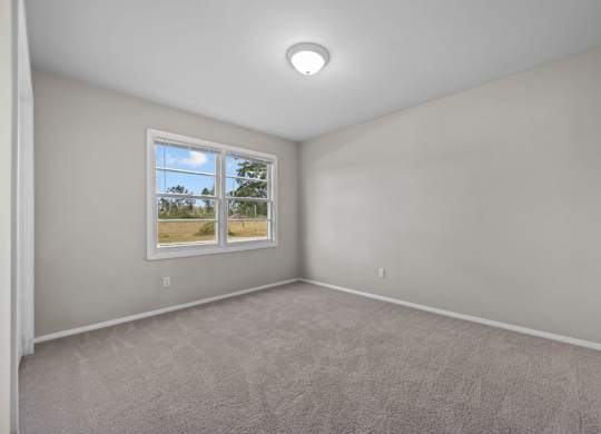 A room with a carpeted floor and a window showing a view of trees and a field.