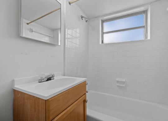 A white bathroom with a wooden vanity and a window.