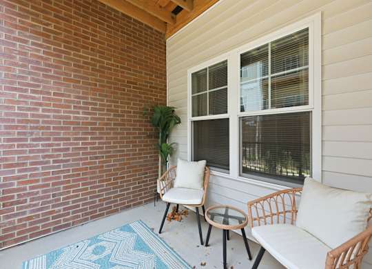 A patio with a white couch, two chairs, and a table with a potted plant.