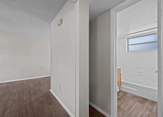 A room with white walls and wooden flooring with a doorway leading to another room.