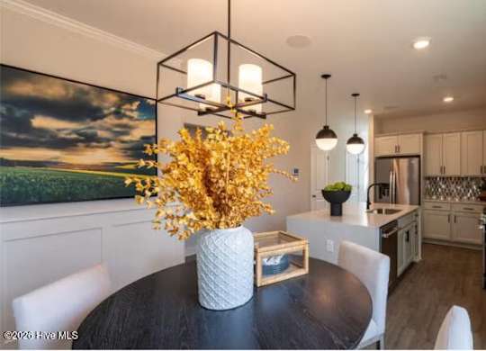 A dining room with a table, chairs, and a vase of flowers.