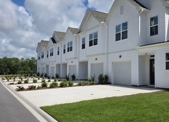 A row of white houses with green lawns in front.