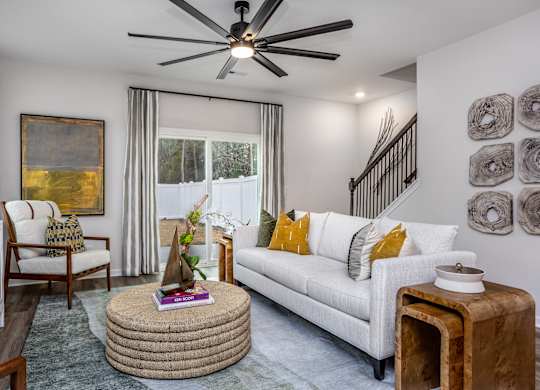 A living room with a white couch, a round ottoman, and a ceiling fan.