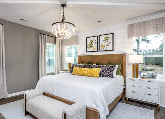 A bedroom with a large bed, a chandelier, and a window with curtains.