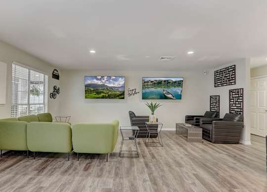 A living room with a green sofa, a grey sofa, a black chair, and a TV mounted on the wall.