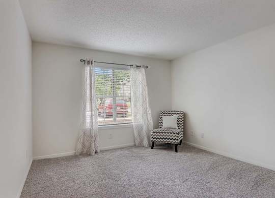 A room with a chair and a window with curtains.