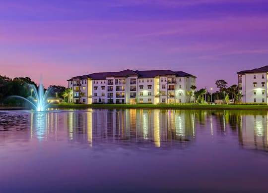 a fountain in a lake with an apartment building at dusk at Inspira, Naples, FL, 34113