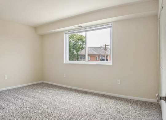 A room with a carpeted floor and a window showing a view of a residential area.