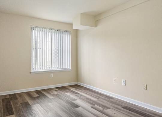 A room with wooden flooring and a window with blinds.