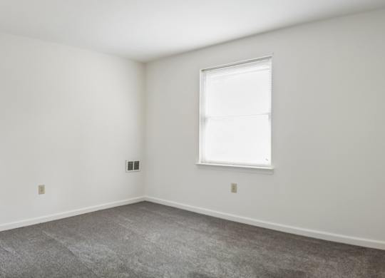 A room with a window and a carpeted floor.