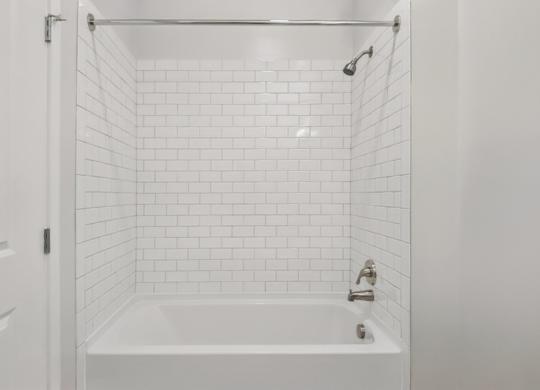 A white bathroom with a white tub and white tiles.