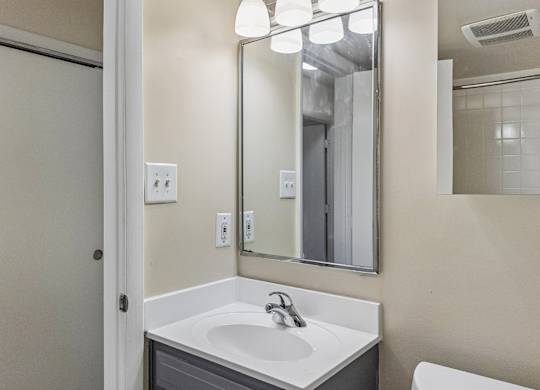 A bathroom with a sink, mirror, and light switches.