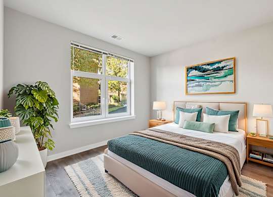 A bedroom with a bed, a potted plant, and a painting on the wall.