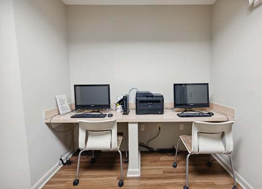 a desk with three computers and a printer on it