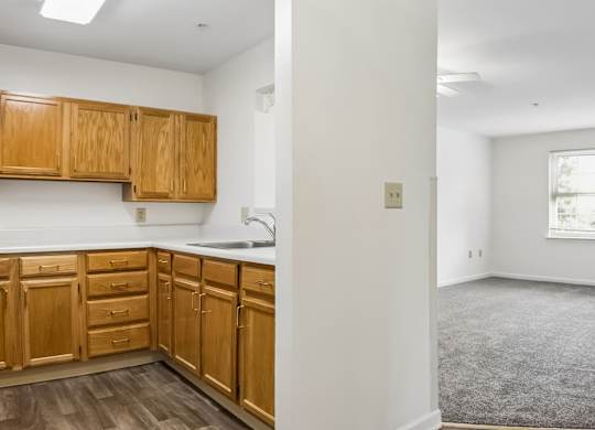 A kitchen with wooden cabinets and a grey carpeted room.