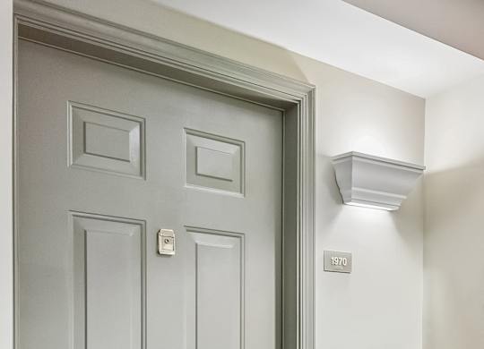 A grey door with a handle and a light switch on the wall.
