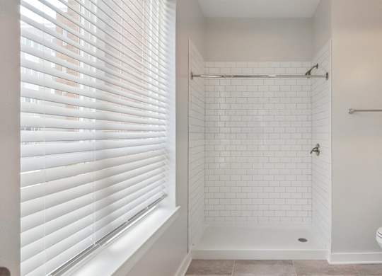 A white bathroom with a toilet, sink, and a shower with a white tile wall.