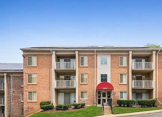 A red brick apartment building with a red awning and a green lawn in front.