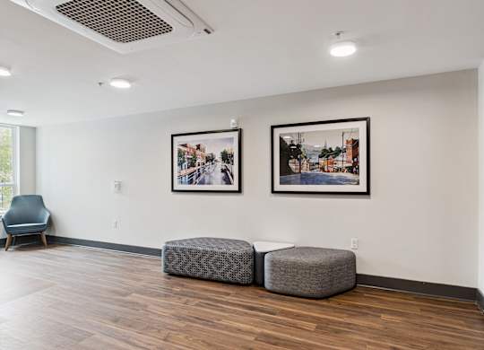A room with two framed pictures on the wall and two round ottomans.