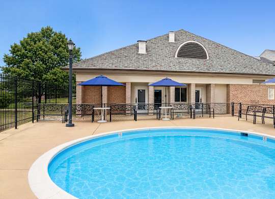 A swimming pool in front of a house with a black fence around it.