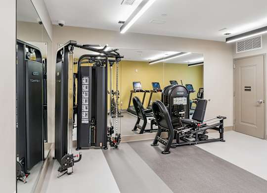 A gym with a variety of equipment including a treadmill, a weight machine, and a rowing machine.