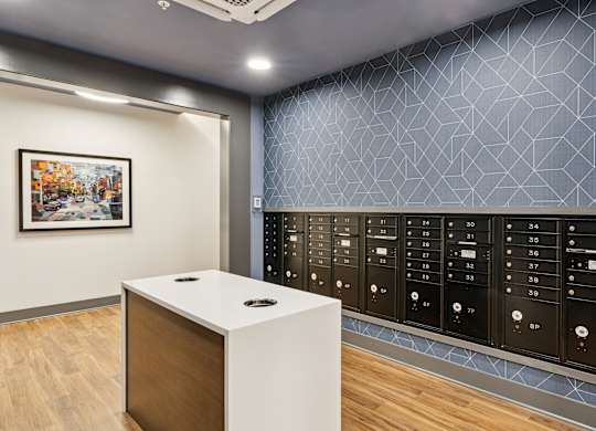 A white reception desk with a black circular object on top is in front of a wall with a framed picture and a row of black lockers.