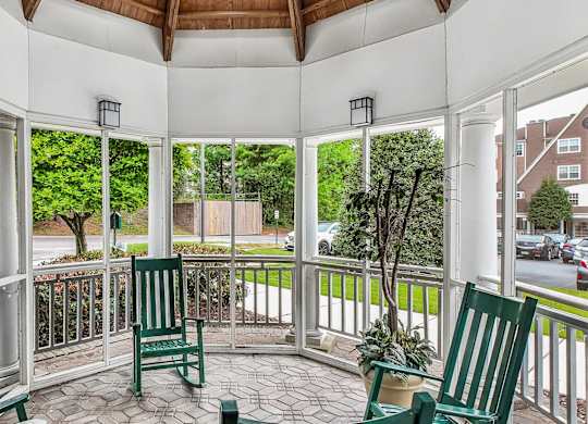 A white gazebo with a wooden roof and a white railing with a green chair and a potted plant.