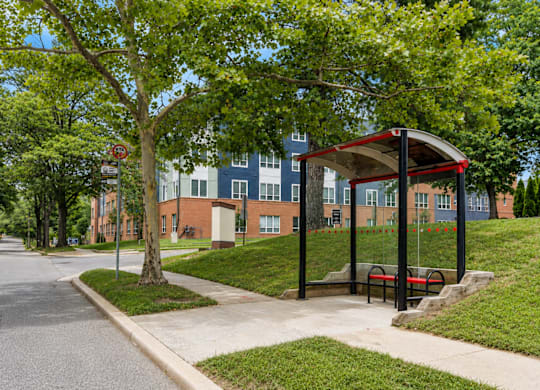A bus stop with a red roof is located on a sidewalk next to a grassy area.