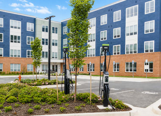 A parking lot with a charging station and a tree in front of a building.