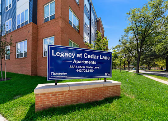 A sign for Legacy at Cedar Lane Apartments is in front of a brick building.