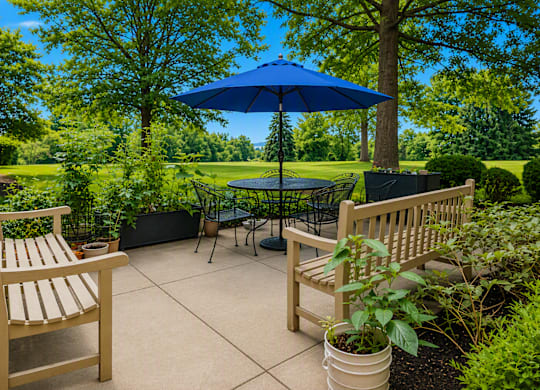 A blue umbrella sits in the middle of a patio with two chairs and a table.