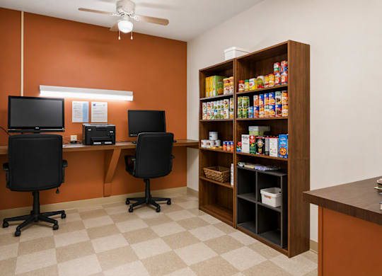 A room with orange walls has two black chairs and a desk with two monitors.
