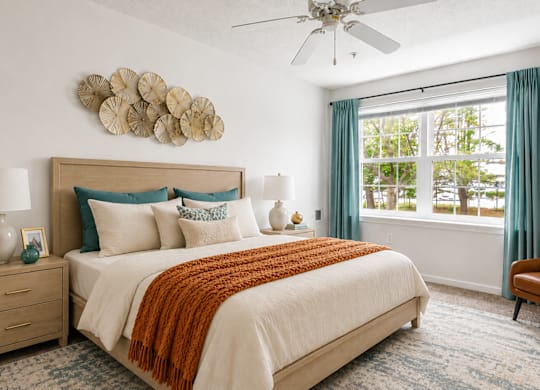 A bedroom with a large bed, a ceiling fan, and a window with blue curtains.