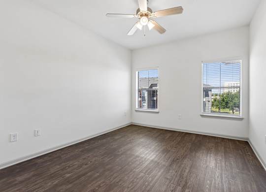 A room with a ceiling fan and two windows.