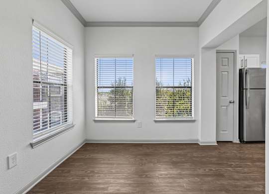 A room with wooden floors and white walls, featuring a refrigerator and a door.