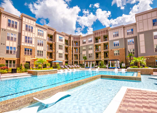 a swimming pool with lounge chairs and umbrellas in front of an apartment building